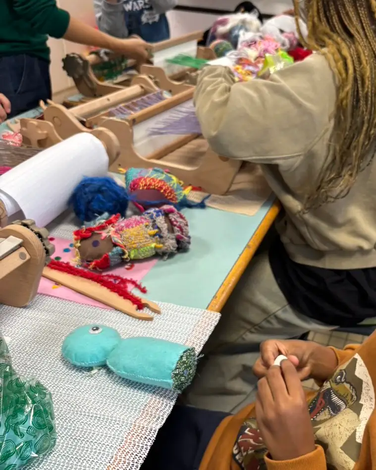 L'atelier de tissage de l'hôpital.
Plusieurs métiers à tisser sont alignés sur la table, et des enfants ayant environ l'âge d'élèves de primaire font du tissage.