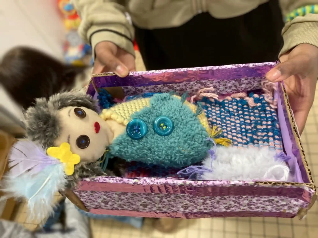 La poupée couchée sur un lit en carton.
Le lit en carton est recouvert d'un joli papier à motifs floraux.